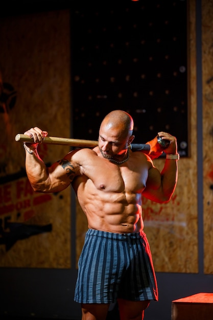 Strong athletic man posing with a sports hammer on the background of the gym. A strong bodybuilder with perfect abs, shoulders, biceps, triceps and chest.