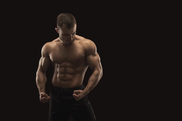 Strong athletic man showing big biceps and muscular body, standing in bodybuilder competitive posture. Studio shot on black background. Bodybuilding concept