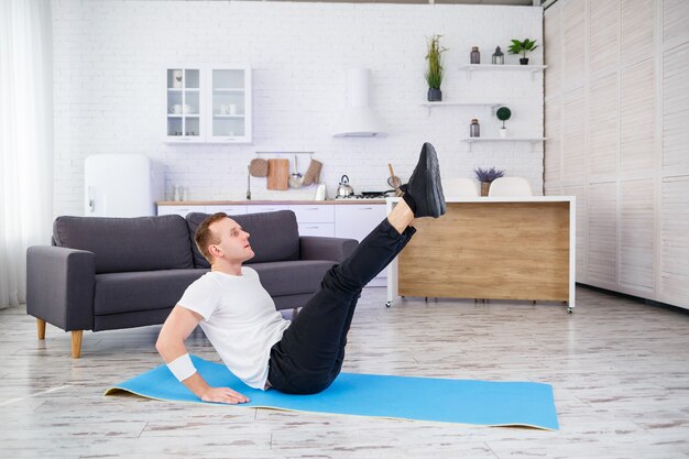 A strong athletic man in a T-shirt and doing press exercises at home in his spacious and bright apartment with a minimalistic interior. Doing sports at home.