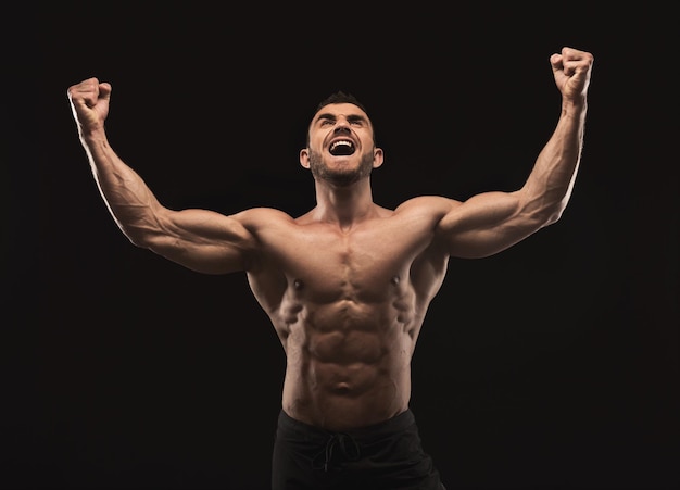 Strong athletic muscular man screaming. Emotional male portrait. Half naked bodybuilder with perfect abs. Fitness model, win and success concept