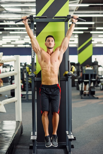 Strong attractive man does pull-up on the crossbar during training in the modern gym. Front view.