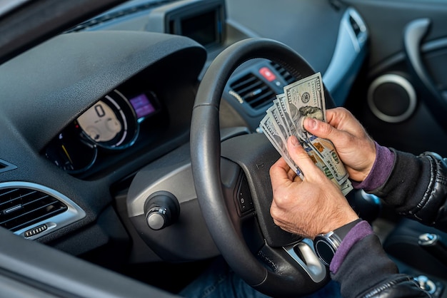 강한 나쁜 범죄자는 차 안에서 많은 양의 달러 지폐를 계산합니다.