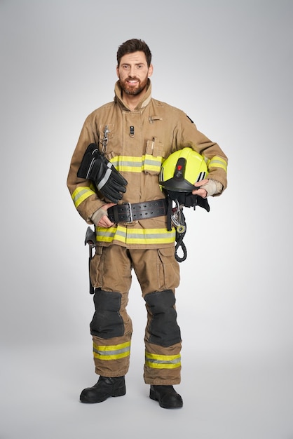 Strong bearded fireman posing to camera with yellow protective helmet front view of happy male