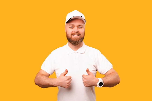 Strong bearded man wearing white T shirt and cap is showing two thumbs up