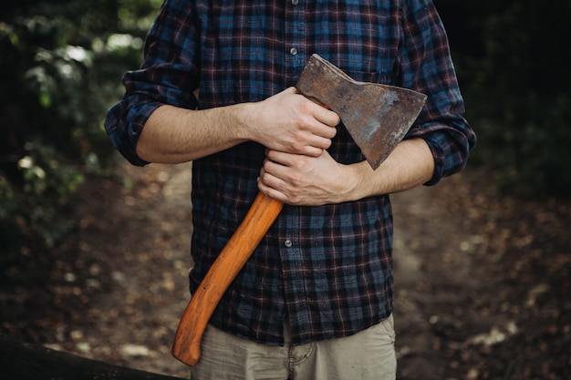 Strong bearded woodcutter holding an ax in the woods 