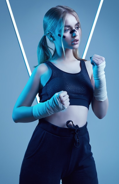 Strong beautiful girl with blonde hair, confident look, fists in protective boxing bandages