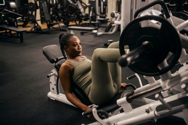 A strong black sportswoman practicing on a leg press machine at gym