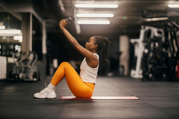 A strong black sportswoman practicing situps with weight plate at the gym