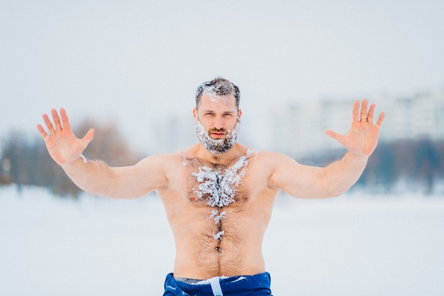 Strong bodybuilder covered with snow posing outdoor in winter snowy day