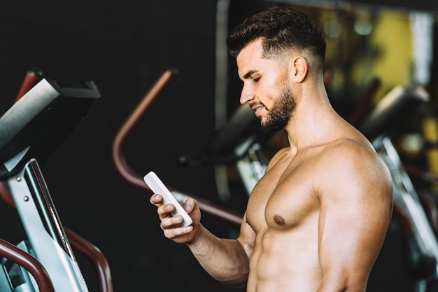 Strong caucasian adult man using a mobile in a gym