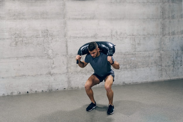 Strong Caucasian sporty man in sportswear lifting Bulgarian training bag.