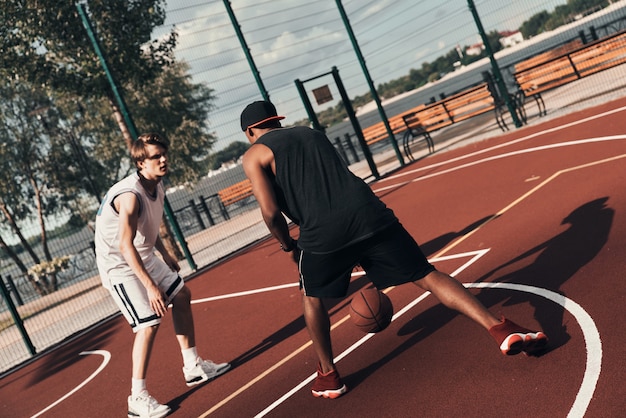 Сильные конкуренты. Двое молодых людей в спортивной одежде играют в баскетбол, проводя время на открытом воздухе
