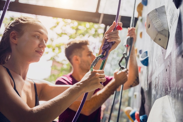 A strong couple of climbers climb an artificial wall with colorful grips and ropes