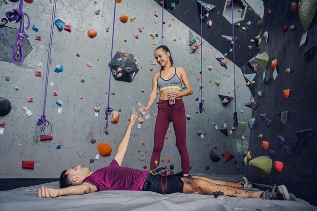 Photo a strong couple of climbers relax near artificial wall with colorful grips and ropes