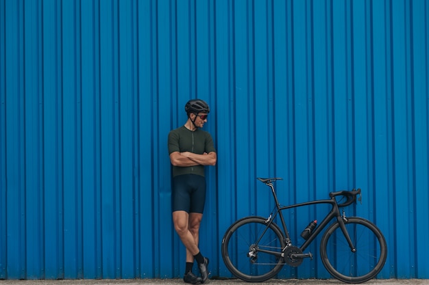 屋外の青い壁の近くに自転車で立っている強いサイクリスト