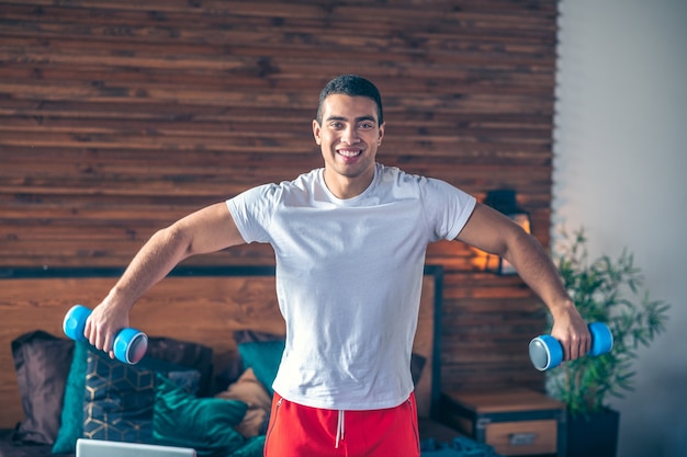 Strong dark-haired man in red shorts holding dumbbells