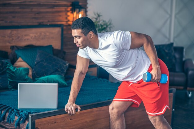 Strong dark-haired man in red shorts working on his biceps