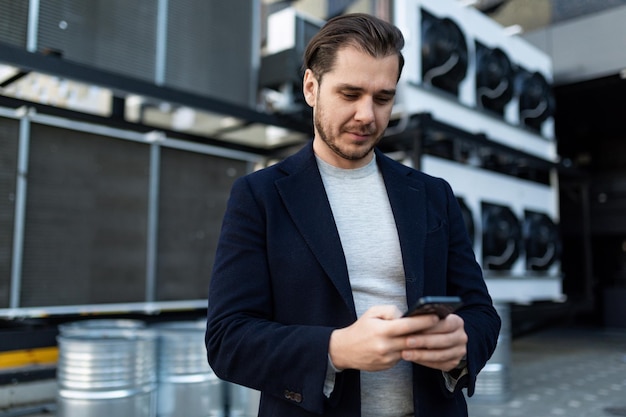 Strong engineer in business clothes on the background of a refrigeration unit with a mobile phone