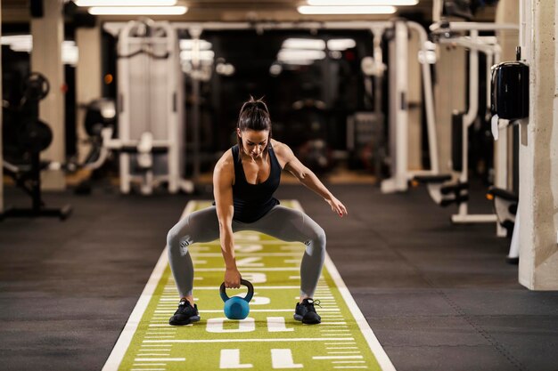 Foto un forte bodybuilder femminile è accovacciato in palestra e solleva kettlebell in palestra