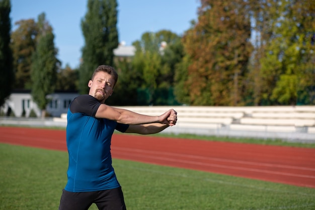 腕を組んでいるストロングフィットの男性は、staduimでのトレーニングの前にウォームアップします。テキスト用のスペース