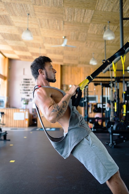 Strong and fit man using trx in gym