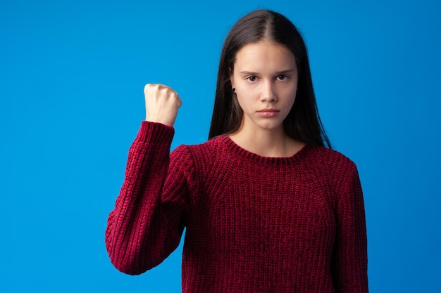 Strong girl showing arm muscle confident and proud of power blue background