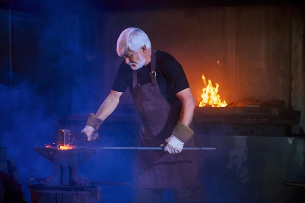 Strong grey haired man processing molten metal on anvil