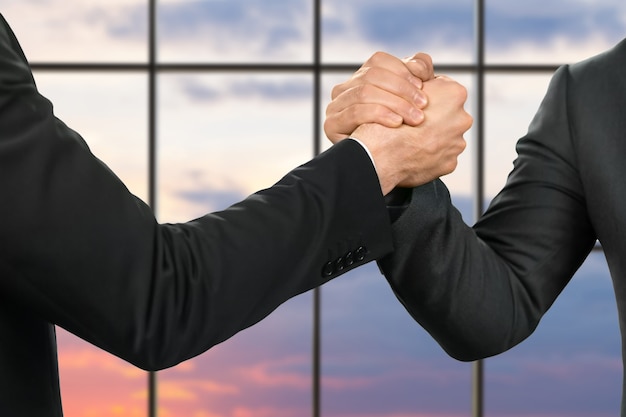 Strong handshake of businessmen. friends' greeting on sunrise background. partnership and protection. strength of a gesture.