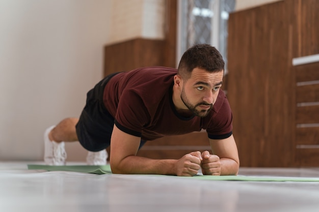 Forte bel giovane che risolve facendo plancia in palestra vuota o casa. sportivo muscoloso che fa esercizi da solo mentre si distanzia o si blocca in palestra. ragazzo determinato che fa allenamento fisico.