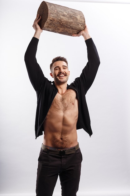 Strong happy young man with moustache and naked torso rise up a tree trunk above the head, over white background.