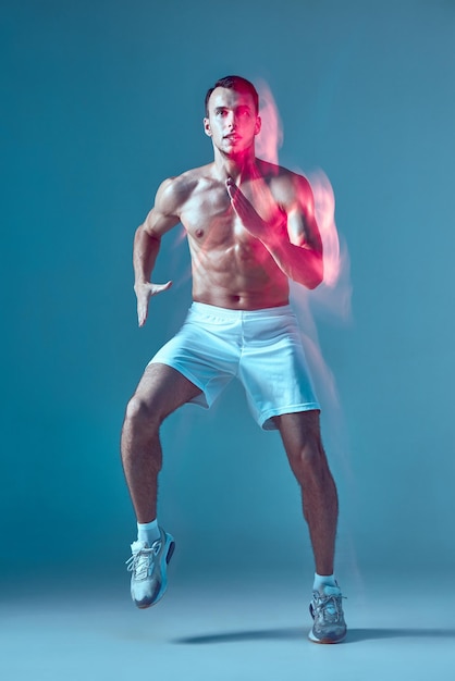 青のスタジオ ライトペインティング効果でズンバ フィットネス トレーニングで強く健康な若い男性