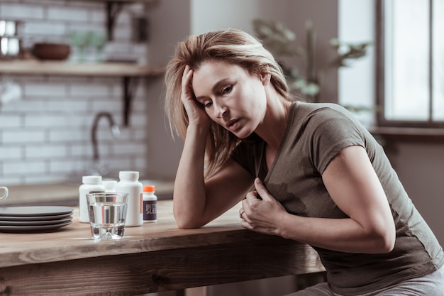 Strong heartache. Blonde-haired depressed mature woman having strong heartache taking pills