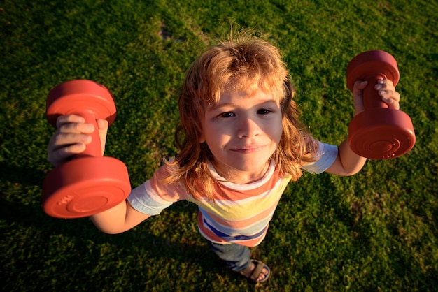 Strong little boy. Funny child face. Sports for development and healthy strong kid with dumbbell exercise.