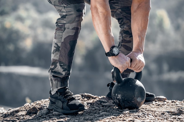 Strong male arms on the kettlebell of 24 kilos Muscular hands with a watch on the weight Bodybuilder's hands and legs close up on the rock