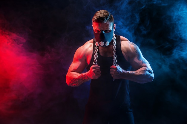 Strong male athlete in a black training mask on a black wall