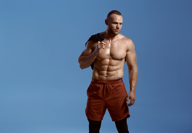 Сильный спортсмен-мужчина, фотосессия в студии, синий фон. один мужчина спортивного телосложения, спортсмен без рубашки в спортивной одежде, активный здоровый образ жизни.