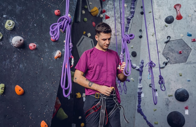 Сильный мужчина-альпинист у искусственной стены с красочными захватами и веревками