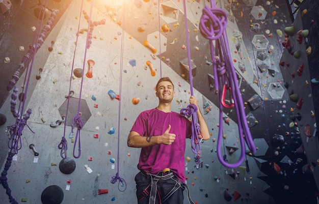 A strong male climber against an artificial wall with colorful grips and ropes