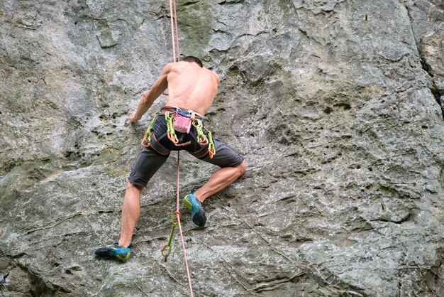 Strong male climber climbing steep wall of rocky mountain. Sportsman overcoming difficult route. Engaging in extreme sports hobby concept.