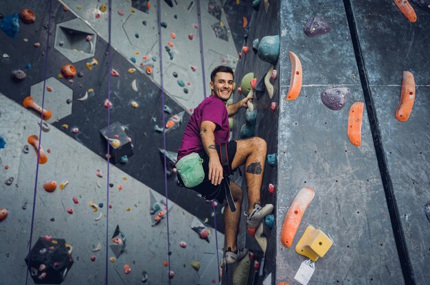 A strong male climber climbs an artificial wall with colorful grips and ropes