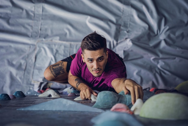 A strong male climber climbs an artificial wall with colorful grips and ropes