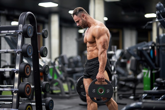 Photo strong man carrying plates for barbell in gym