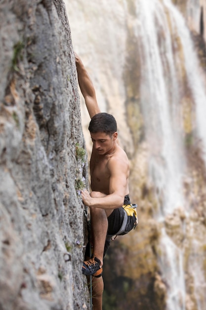 Foto uomo forte che si arrampica su una montagna con equipaggiamento di sicurezza