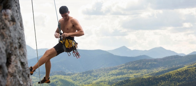 Foto uomo forte che si arrampica su una montagna con equipaggiamento di sicurezza