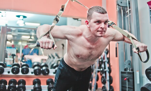 Strong man does crossfit push ups with fitness straps at gym