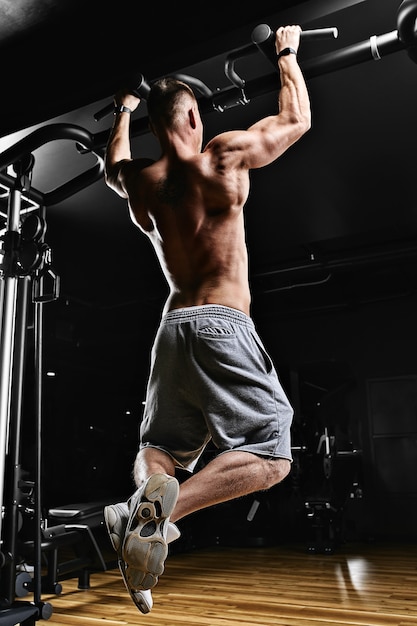 Strong man doing pull-ups on a bar in a gym.