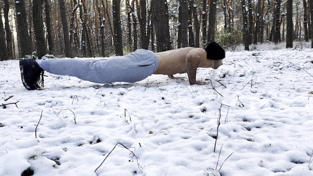 Strong man doing push ups on snow at winter forest Sportsman exercis at nature Young guy training