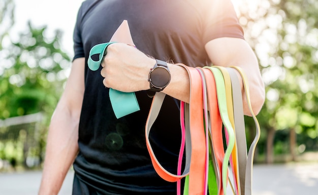 Photo strong man guy holding set of colorful elastic rubber bands at the stadium outdoors. athlete male person during workout with additional sport equipmant