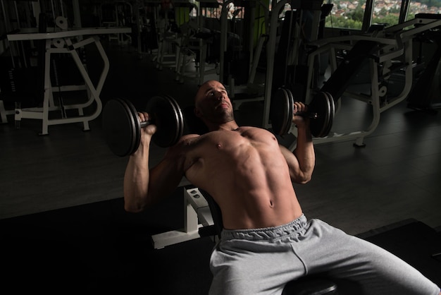 Сильный человек в тренажерном зале и тренирует грудь с гантелями Мускулистый спортивный бодибилдер Фитнес-модель Упражнения