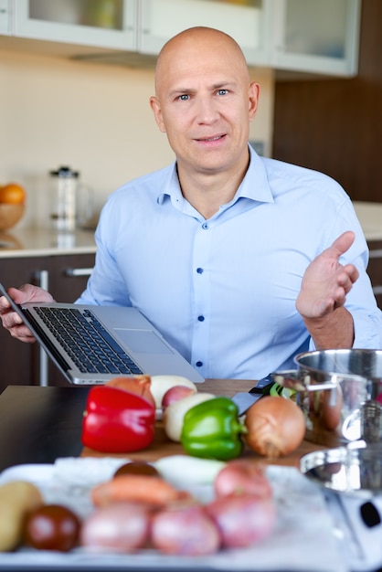 strong man in kitchen preparing food and uses laptop